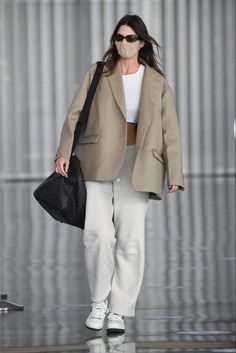 a woman walking down the runway wearing a face mask and carrying a black handbag