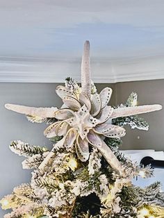 a decorated christmas tree with white flowers and green leaves on the top, in a living room