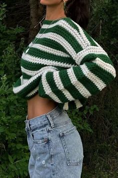 a woman wearing a green and white knitted sweater standing in front of some trees