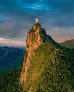 a person standing on top of a mountain with a cross at the top in the distance