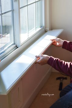 a woman sitting in front of a window with her hands on the edge of the window sill