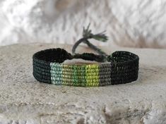 a green and yellow bracelet sitting on top of a stone wall next to a plant