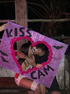 a man kissing a woman in front of a pink sign that says kiss cam on it