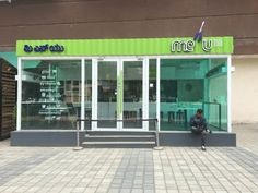 a person sitting on a bench in front of a building with green and white lettering