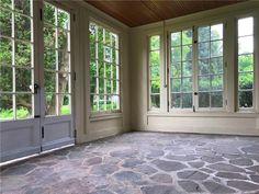 an empty room with large windows and stone flooring in front of the door to another room