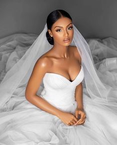 a woman in a white wedding dress sitting on a bed wearing a veil over her head