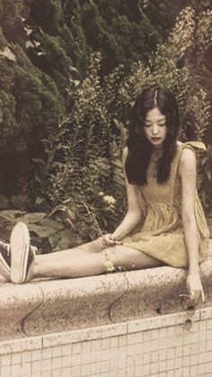 a young woman sitting on the edge of a swimming pool with her legs crossed, looking down