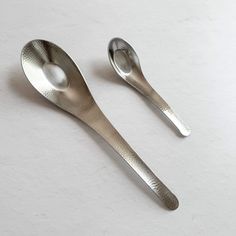 two silver spoons sitting next to each other on a white surface