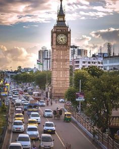 a large clock tower towering over a city filled with traffic on a busy street at sunset