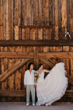 a bride and groom standing in front of a wooden barn door holding each other's hand