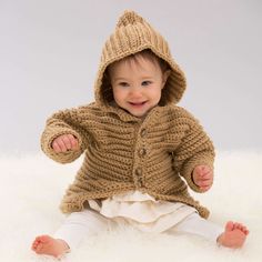 a baby wearing a brown knitted jacket and white pants sitting on a fluffy rug