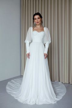 a woman in a white wedding dress standing next to a window with curtains behind her