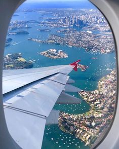 an airplane wing is seen through the window as it flies over water and cityscapes