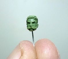 a person holding a tiny green head on top of a toothpick in their left hand