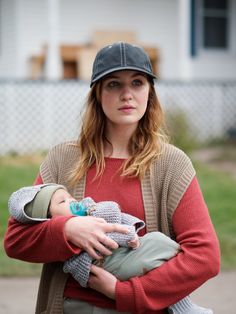 a woman holding a baby in her arms while wearing a baseball cap and red sweater