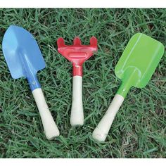 three plastic shovels and spatulas laying on the green grass in front of each other