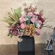 a vase filled with lots of flowers sitting on top of a table next to a statue