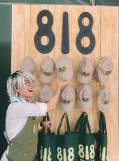 a woman with white hair is pointing at the numbers on a wooden sign that has hats hanging from it