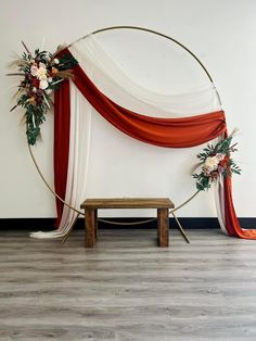 an arch decorated with red and white draping, flowers and greenery sits in front of a wooden bench