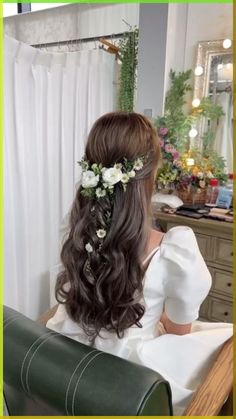 a woman sitting in a chair with long hair and flowers in her hair, looking at herself in the mirror