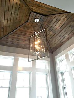 a chandelier hanging from the ceiling in a room with three windows and wood paneling