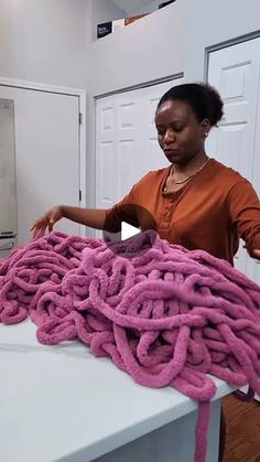 a woman in an orange shirt is doing something with pink yarn on a white table