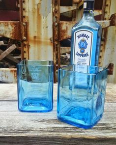 two blue glass tumblers sitting on top of a wooden table next to a bottle