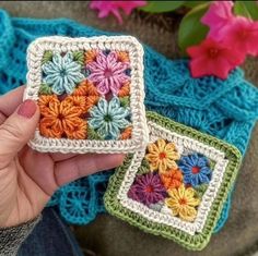 someone is holding two small square crocheted coasters