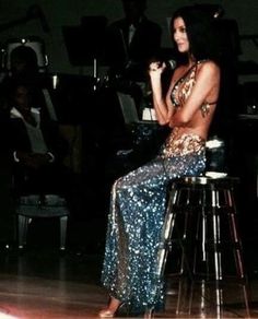 a woman sitting on top of a stool in front of a piano and orchestra behind her