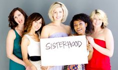 four women in dresses holding a sign that says sisterhood written on the front and side