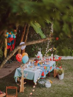 an outdoor birthday party with balloons, cake and confetti on a table in the grass