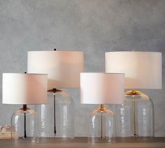 three clear glass lamps sitting on top of a wooden table next to a lamp shade