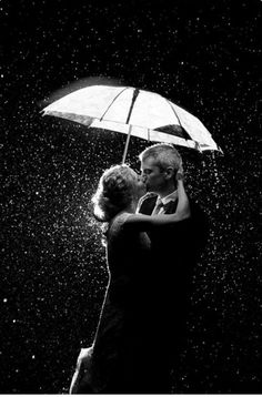 black and white photograph of two people under an umbrella in the rain, hugging each other