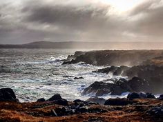 an ocean view with waves crashing on the rocks and dark clouds in the sky above