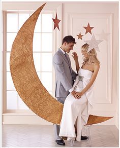 a man and woman standing next to each other in front of a large crescent moon