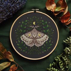 a cross - stitch project with leaves and plants surrounding it on a green surface,