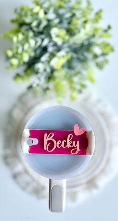 a pink name tag on a white surface next to a potted plant with green leaves