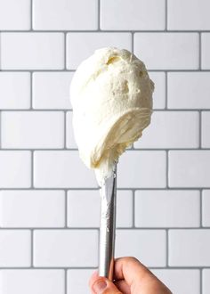 a hand holding a scoop of ice cream over a white brick wall with a silver spoon