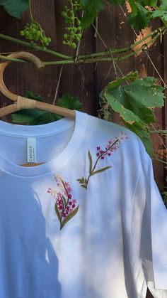 a white t - shirt with pink flowers on it hanging from a wooden hanger