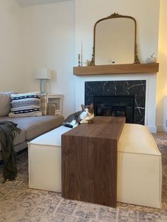 a cat laying on top of a wooden table in front of a couch and fireplace