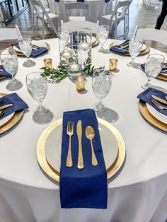 a white table with blue napkins and gold place settings is set for an event