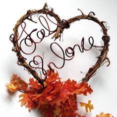 the word love is written on a heart - shaped piece of wire next to autumn leaves