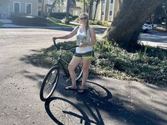 a woman standing next to her bike on the street in front of a tree and house