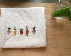 four carrots embroidered on a white towel next to a vase with green plants in it