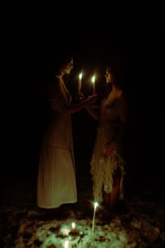 two women standing in the dark holding candles