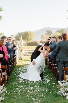 a bride and groom kiss as they walk down the aisle at their outdoor wedding ceremony