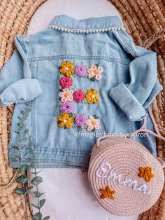 a blue jean jacket with flowers on it and a pink purse sitting next to it