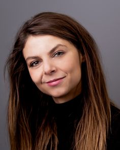 a woman with long brown hair smiling at the camera while wearing a black turtle neck sweater