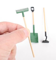 a hand holding a toothbrush next to two small rakes and a green brush