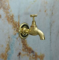 a gold faucet on the side of a wall with rusted walls behind it